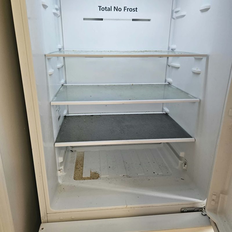 The inside of a fridge before cleaning, with crumbs across the shelf and staining on the base.