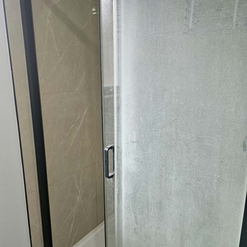 A shower screen before cleaning, the glass clouded over with soap scum and hard water.