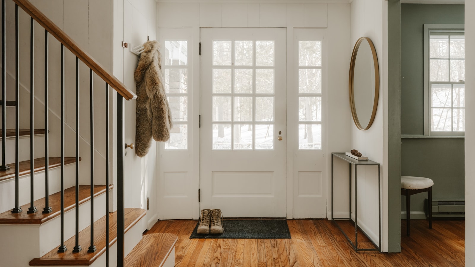 A cottage entryway with a glass-panelled front door, wooden stairs and snow outside.