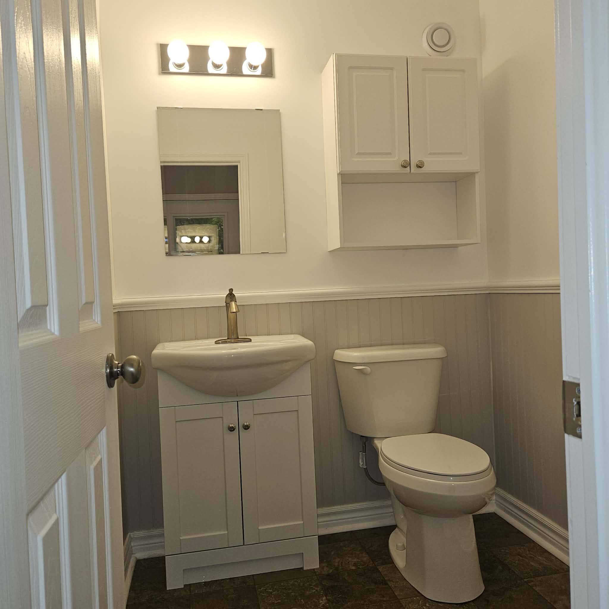 A small bathroom with beadboard panelling, the sink, toilet and floor freshly cleaned.