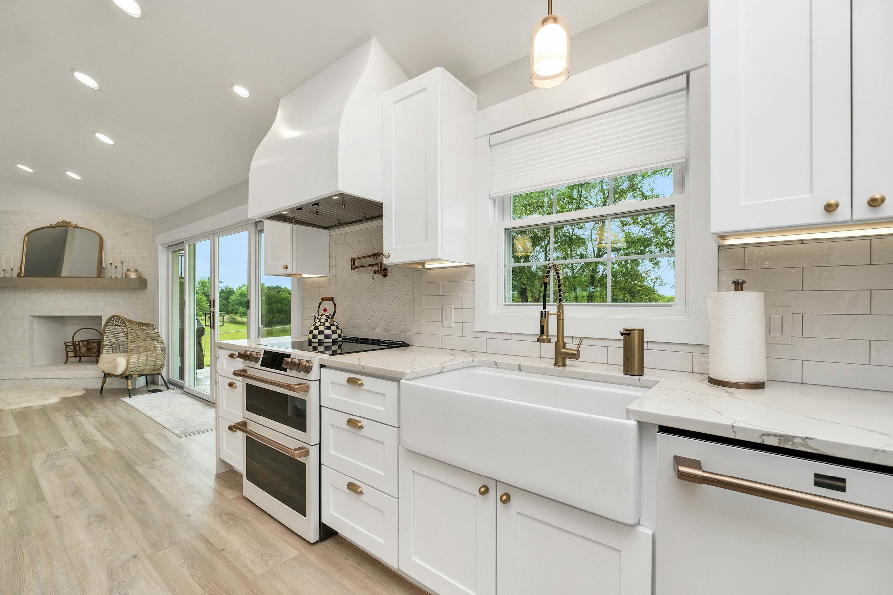 A bright white kitchen with a farmhouse sink and brass taps, looking out to the garden.